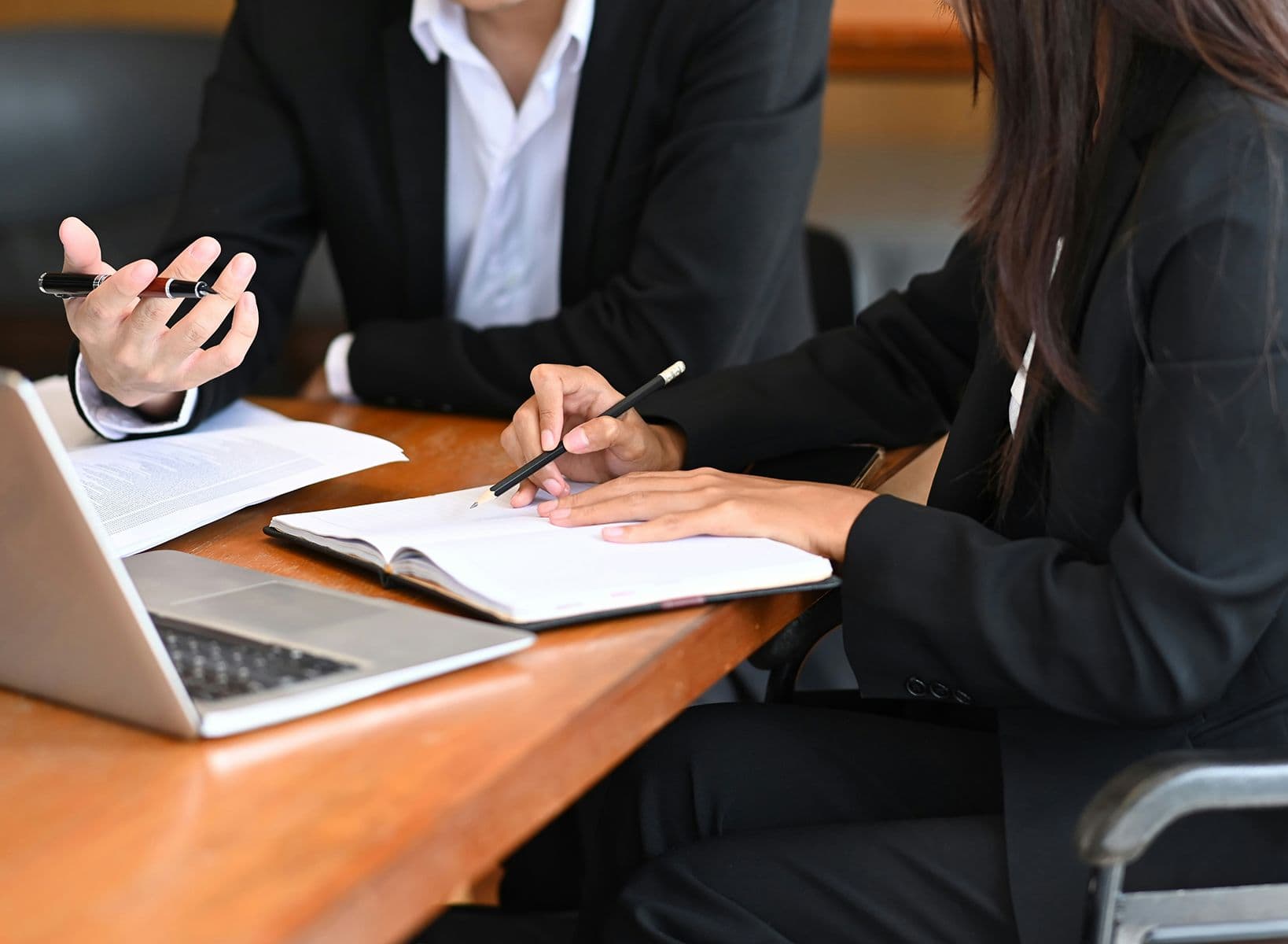 Deux femmes en réunion dans une salle de conférence, discutant avec un ordinateur portable et un bloc-notes sur la table.