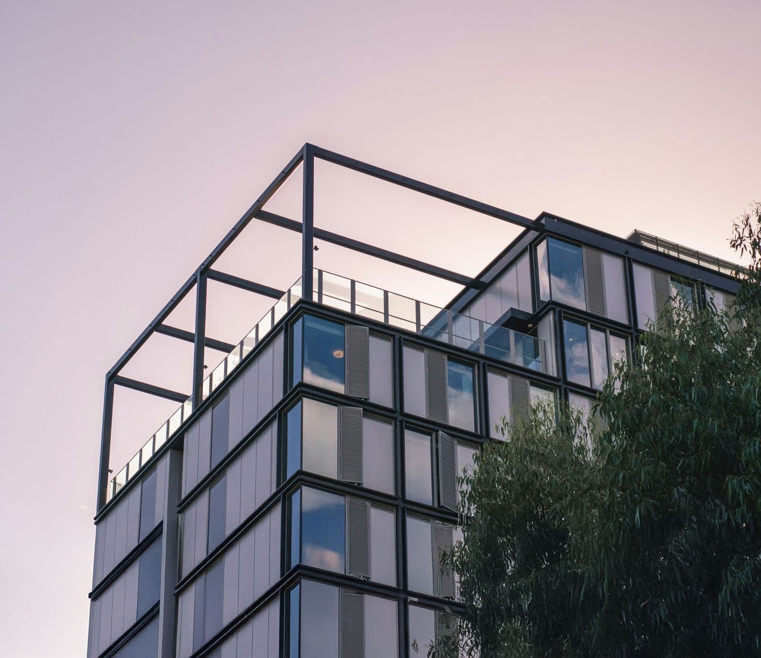 Façade d’un immeuble moderne en verre et métal avec structure ouverte sur le toit, vue au coucher du soleil.